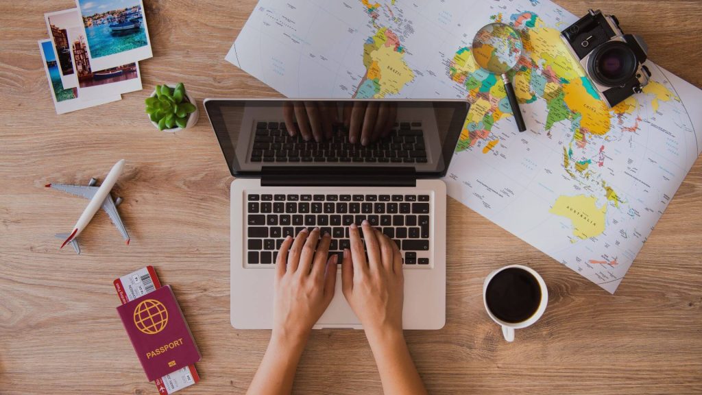 Hands typing on a laptop with a world map, passport, and coffee — planning a family travel budget.