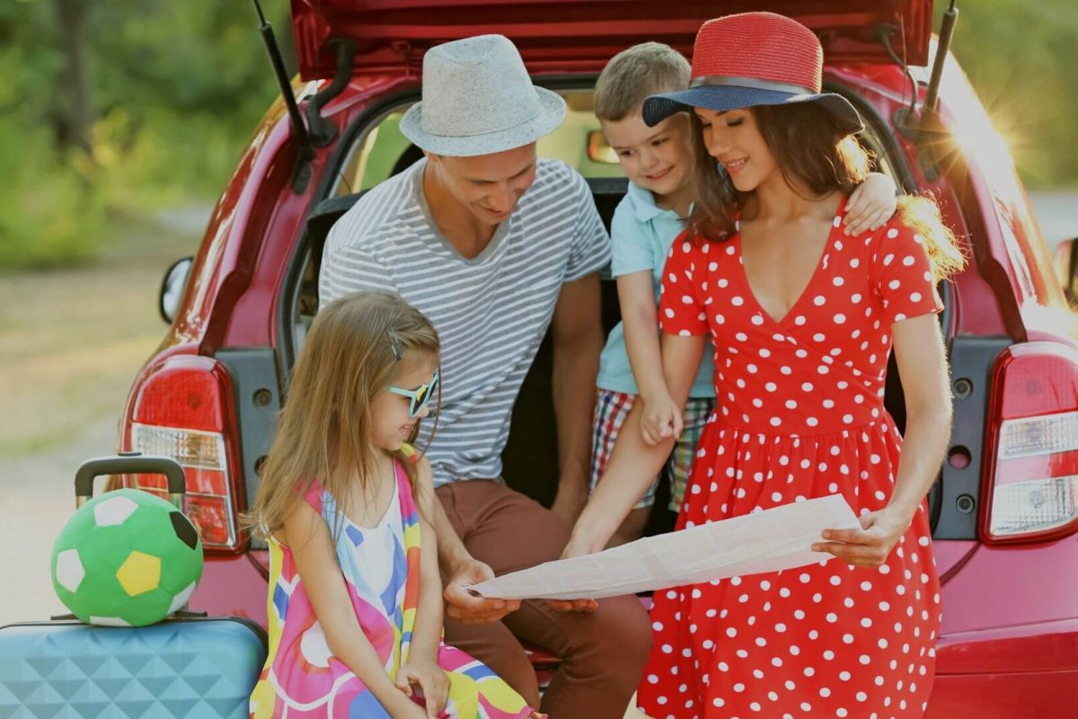 Family preparing for a UK road trip, reading a map beside their car with kids and luggage.