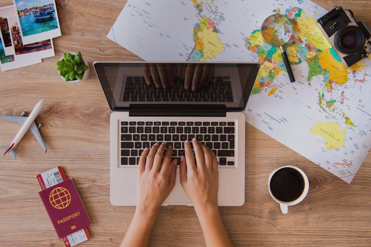 Hands typing on a laptop with a world map, passport, and coffee — planning a family travel budget.